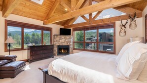 Un dormitorio con chimenea de piedra, ventanas amplias, una cama, un aparador y un televisor.
