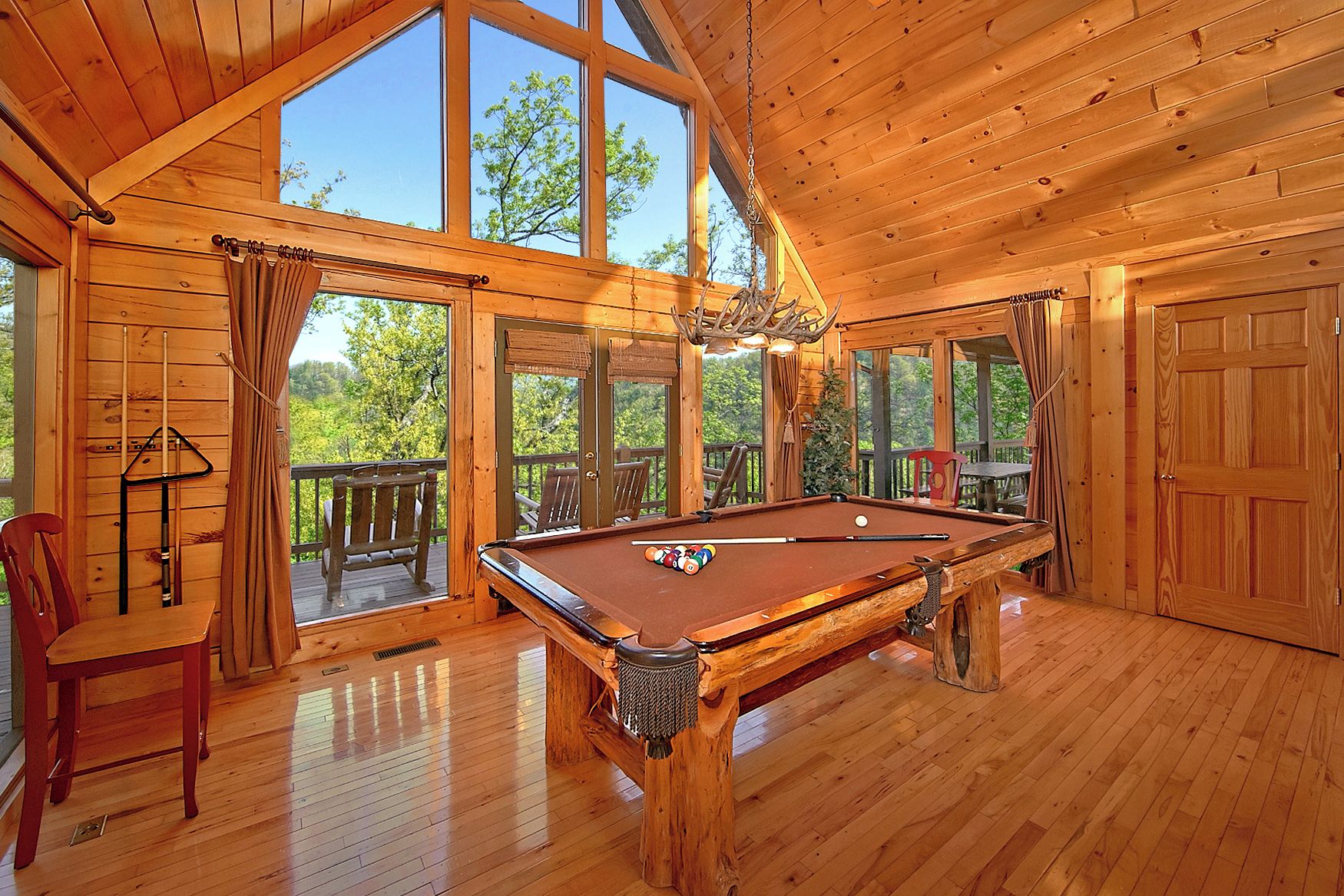 Une table de billard en bois se trouve dans une pièce dotée de grandes fenêtres et d’un balcon.
