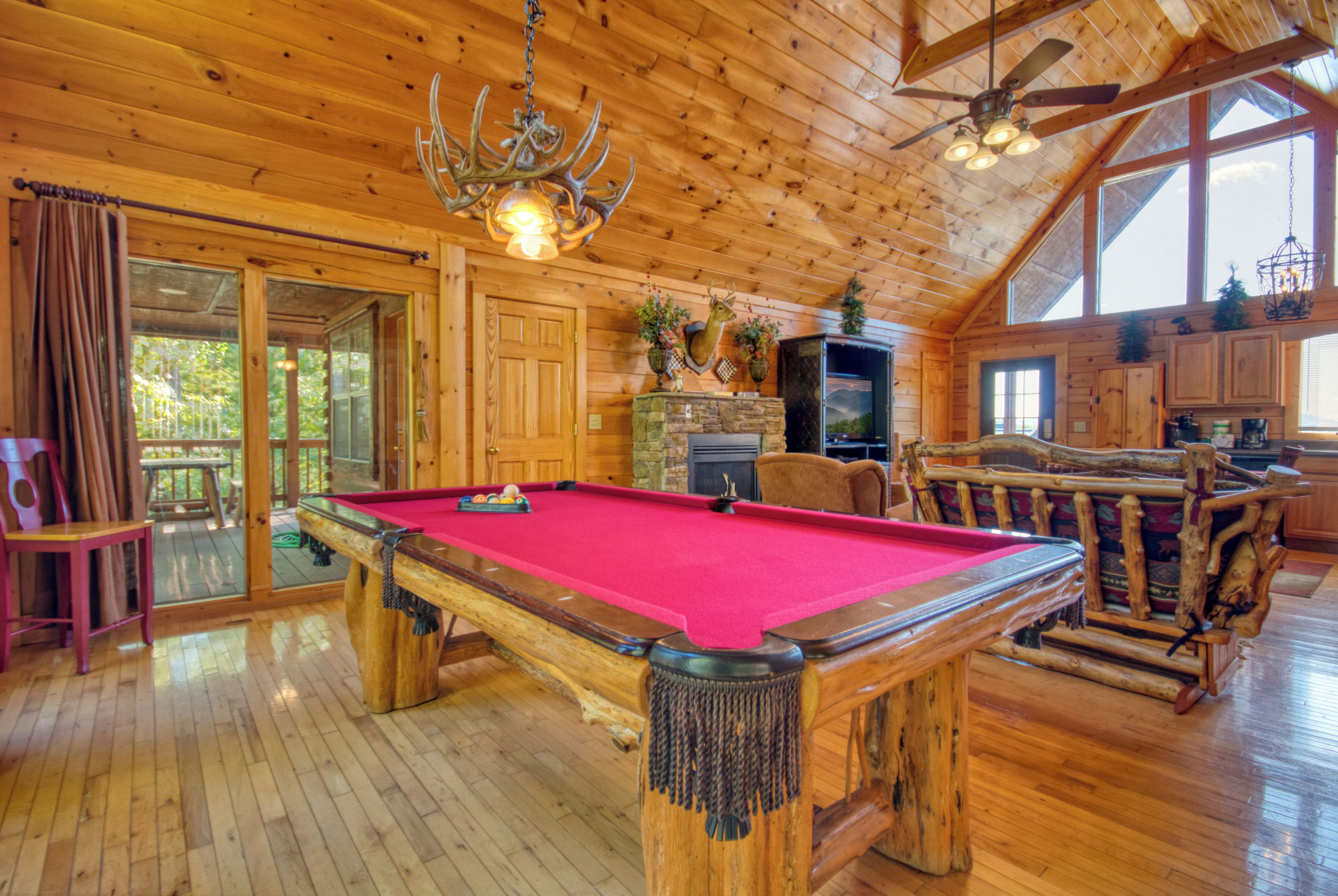 A wooden cabin interior with a pool table, a fireplace, and a large window.