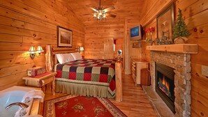 A cozy log cabin room with a bed, a fireplace, a television, and a wooden ceiling. - View of Dollywood’s Fireworks|Pool Table|Hot Tub (SEVIERVILLE)