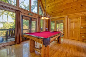 A wooden pool table in a room with large windows and a wooden ceiling.
