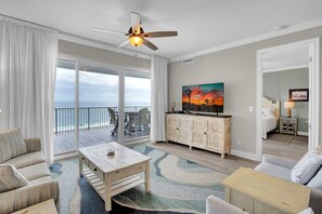 A spacious living room with a large sliding glass door leading to a balcony, a ceiling fan, a dining area, and a view of the ocean. - Regency Isle 911 by Liquid Life (Orange Beach)