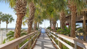 A wooden boardwalk with palm trees on both sides, leading to a beach. - Regency Isle 911 by Liquid Life (Orange Beach)