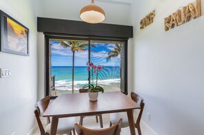 Enjoy meals with a view of the ocean and palm trees from this dining area with a large table and chairs.