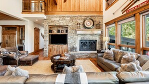 A spacious living room with a stone fireplace, leather sofas, and a large television. - Pristine Mountain Home. Perfect for Families - Hot Tub, Media Room & Elevator (Park City)