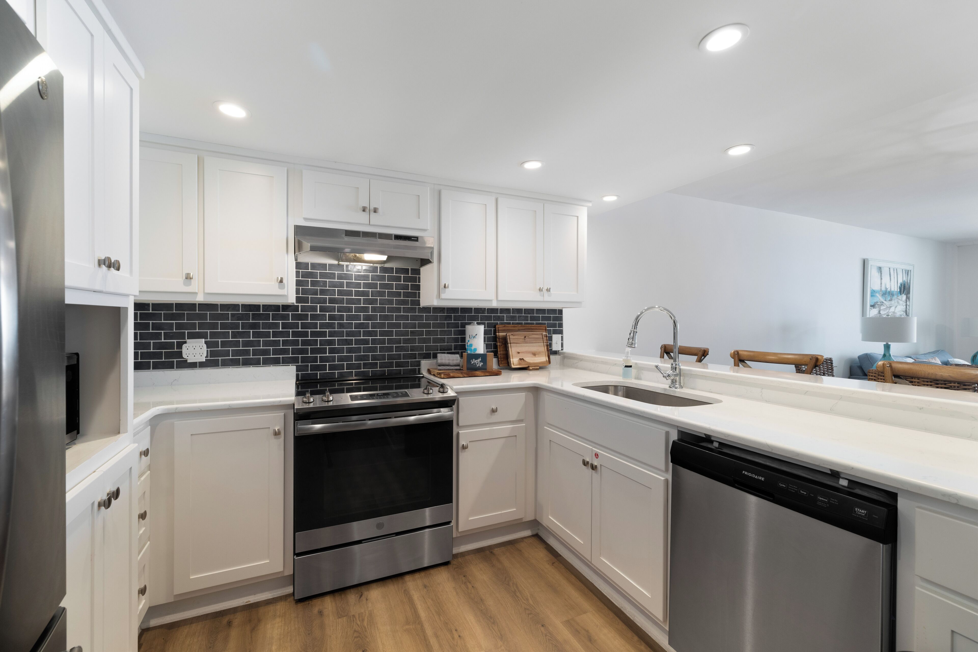 A modern kitchen with white cabinets, a black tiled backsplash, stainless steel appliances, and a wooden countertop.