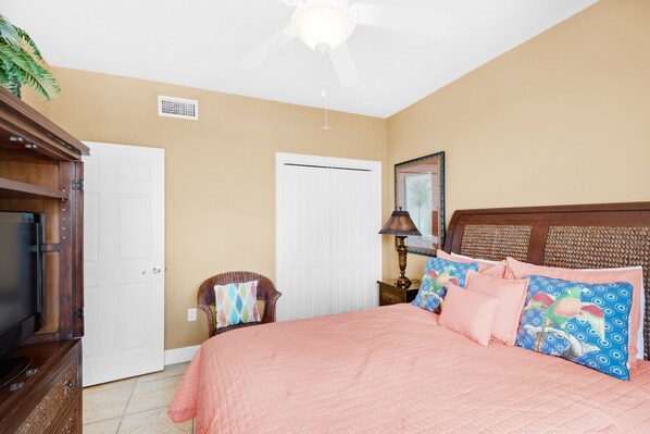 A bedroom with a bed, a television, a ceiling fan, and a door.