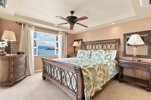 A bedroom with a bed, a ceiling fan, a dresser, a nightstand, and a window with a view. - Your Refreshing Escape by the Ocean! Marvelous Views - Royal Mauian 209 (Kihei, Maui)