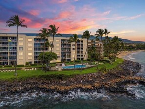 A beachfront hotel with multiple floors, a swimming pool, and palm trees.