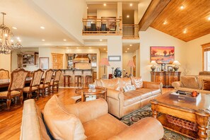 A spacious living area with leather sofas, a dining table, and a kitchen in the background. - Modern Mountain Design, High-End Kitchen, Theater Room & Hot Tub! (Park City)