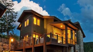 A two-story log cabin with a stone foundation, a balcony, and a stone wall on one side. - Modern Mountain Design, High-End Kitchen, Theater Room & Hot Tub! (Park City)