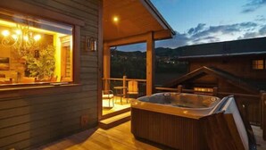 A wooden cabin with a hot tub, a balcony, and a view of the mountains. - Modern Mountain Design, High-End Kitchen, Theater Room & Hot Tub! (Park City)