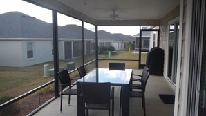 Een overdekt terras met een glazen tafel en stoelen, met uitzicht op omliggende huizen en heuvels.
