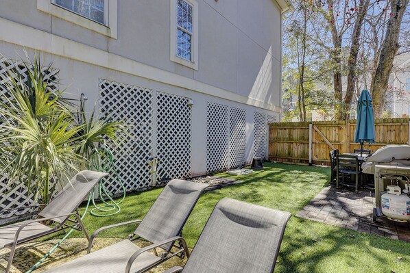 Un patio trasero con una casa blanca, una cerca de madera, césped y muebles de exterior.