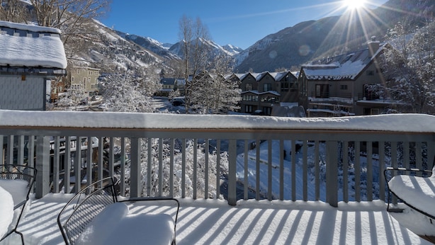 Ein mit Schnee bedeckter Balkon mit Blick auf ein Bergdorf und einen klaren Himmel.