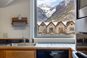 A kitchen with a Bosch dishwasher, wooden cabinets, a built-in sink, and a window overlooking a mountain landscape.