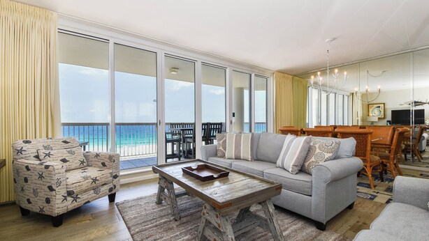 A spacious living area with a large sliding glass door leading to a balcony, a grey sofa, a patterned armchair, and a wooden coffee table. - Nautical-themed beachfront getaway w/private balcony! 🌊 (Destin)