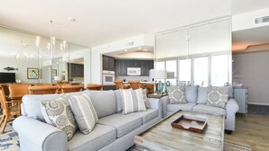 A spacious living room with a grey sofa, a wooden coffee table, and a kitchen area in the background. - Nautical-themed beachfront getaway w/private balcony! 🌊 (Destin)
