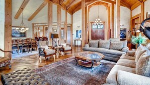 A spacious living room with wooden beams, a large sofa, a coffee table, and a dining area with chairs and a table.