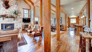 A spacious living room with a stone fireplace, wooden beams, and a large TV.