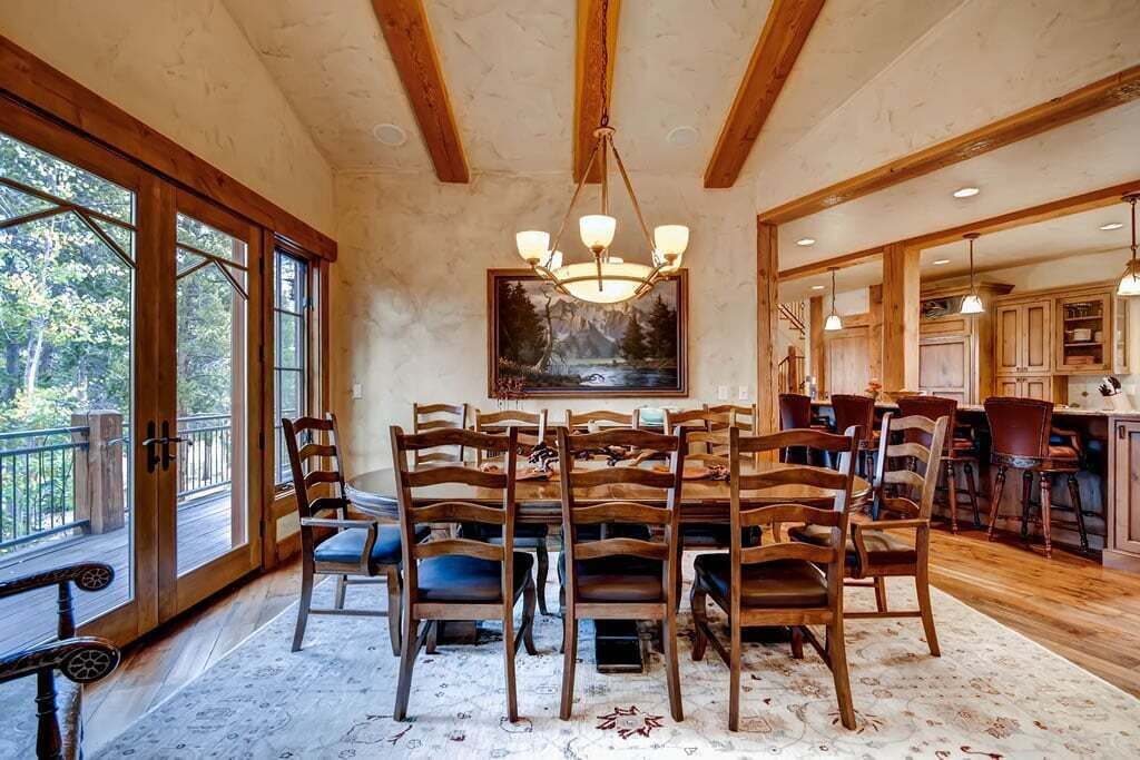 Comedor con sillas de madera, una araña y ventanas amplias con vistas al exterior.