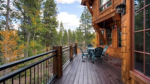 A wooden cabin with a deck, surrounded by trees.