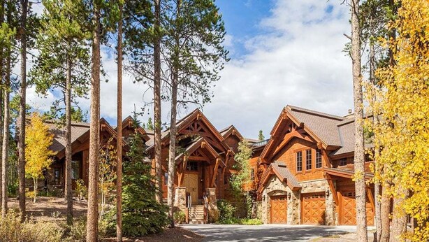 A lodge with multiple wooden cabins, a central entrance, and a driveway surrounded by tall trees.