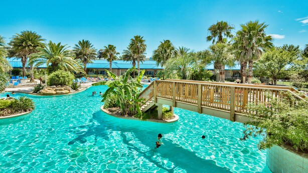 A swimming pool with clear blue water, surrounded by palm trees and a wooden deck. - Paradise at the Palms * Summer Specials! Book Now! 2 King Beds~2 Full Baths! (Destin)