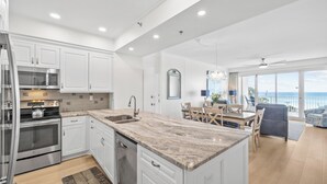 A modern kitchen with white cabinetry, stainless steel appliances, and a large island with a marble countertop.