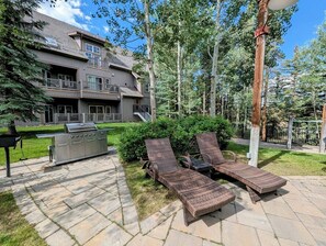 A patio with two wicker lounge chairs, a barbecue grill, and a stone pathway leading to a building with a balcony. - Summer Getaway | Pool,  Hot Tub + Mini Golf (Keystone)
