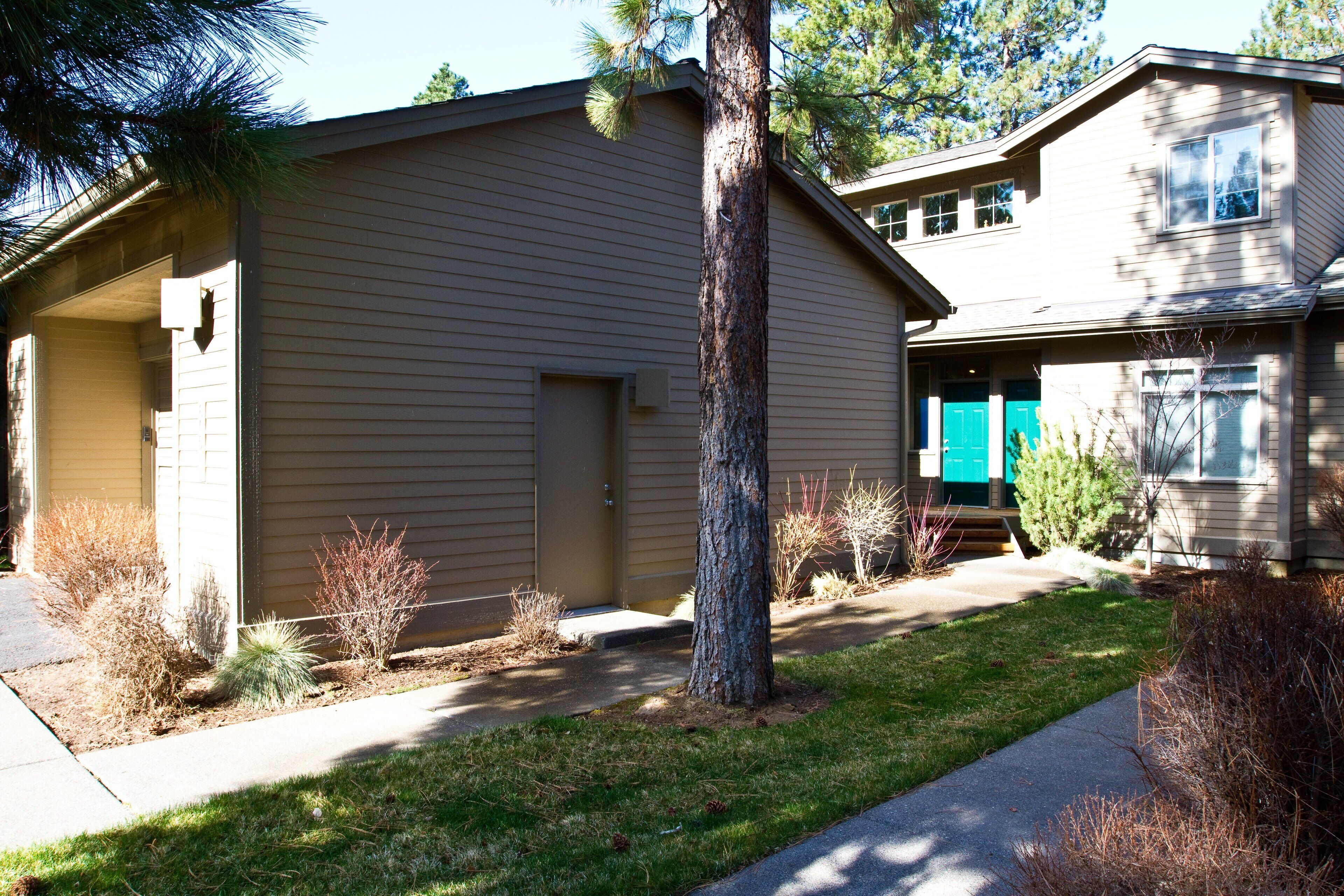 A two-story house with a garage, a front yard with a tree, and a small shrubbery.