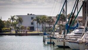 A marina with several boats docked, a building with a white facade, and palm trees in the background.