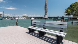 A wooden dock with a bench, a tall striped monument, and a marina with boats in the background.