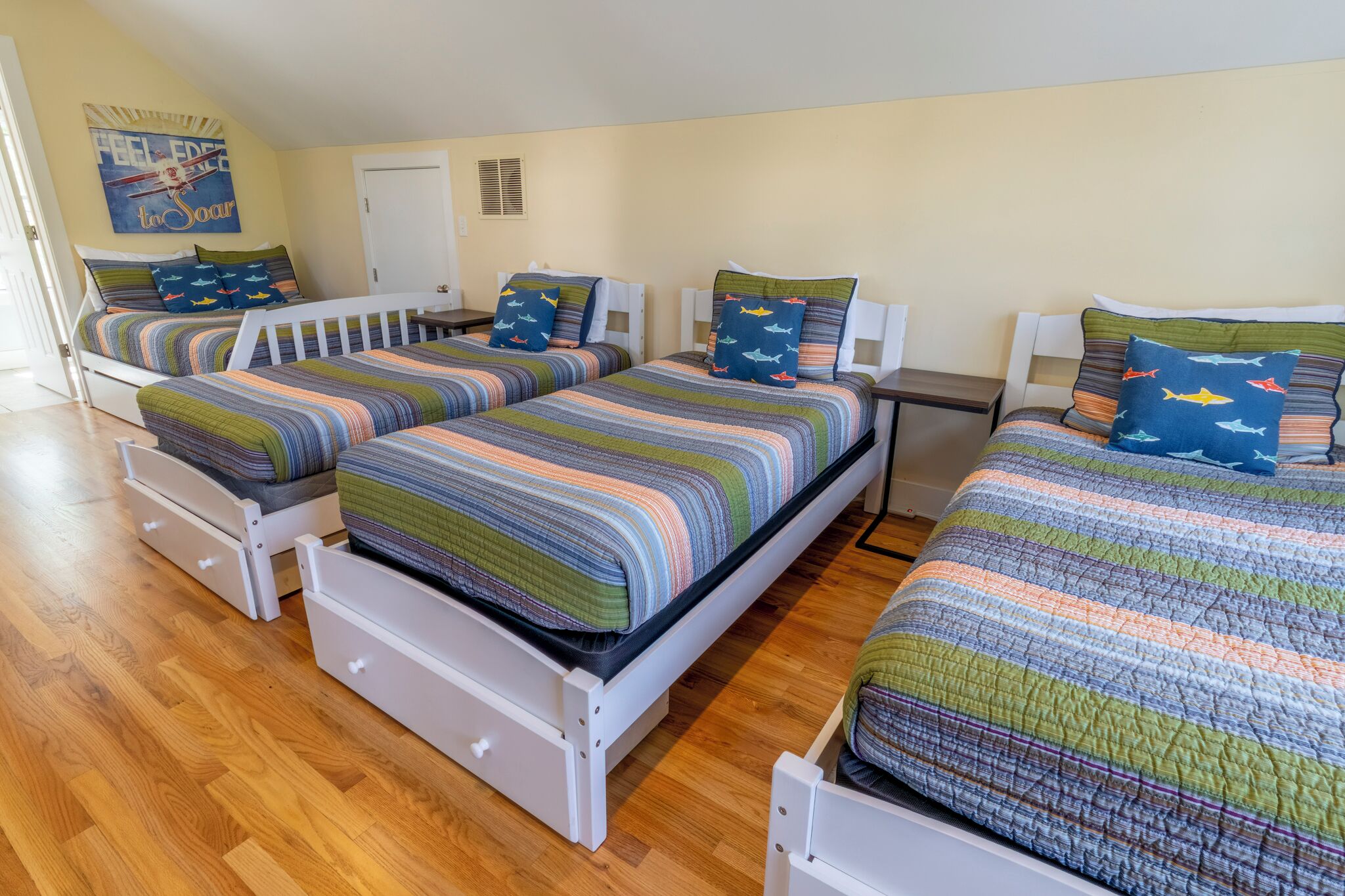 A room with four beds, each with striped bedding and matching pillows, in a simple, functional layout.