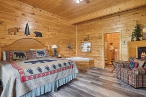 A log cabin bedroom with a bed, a fireplace, a wooden floor, and a plaid sofa.