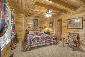 Ein gemütliches Schlafzimmer in einer Holzhütte mit einem Bett, einem Sessel, einem Deckenventilator und einem gerahmten Bild an der Wand.