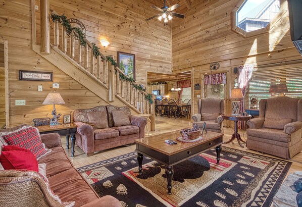 A cozy log cabin interior with a staircase, wooden walls, a dining area, and a living room furnished with sofas and a coffee table.