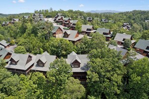 A cluster of log cabins surrounded by dense forest, with multiple buildings visible in the background.