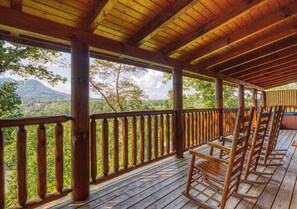 A wooden deck with a railing, wooden chairs, and a view of a mountainous landscape.