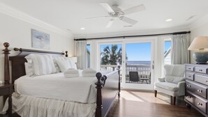 Una camera da letto con un letto grande, una ventola a soffitto, vista sull'oceano e un balcone con una sedia.