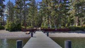A wooden pier leading to a dock, surrounded by tall pine trees and a clear water body.