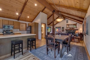Une cuisine spacieuse avec des meubles en bois, un îlot central doté de tabourets, un coin repas avec une grande table et des chaises, et une cheminée en pierre.