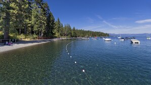 A clear lake with boats, a sandy beach, and a forested area.