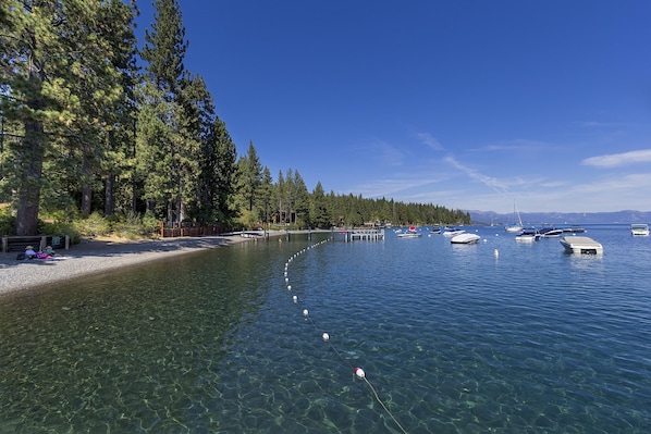 Un lac aux eaux limpides où l’on peut naviguer, une plage de sable et une rangée d’arbres imposants.