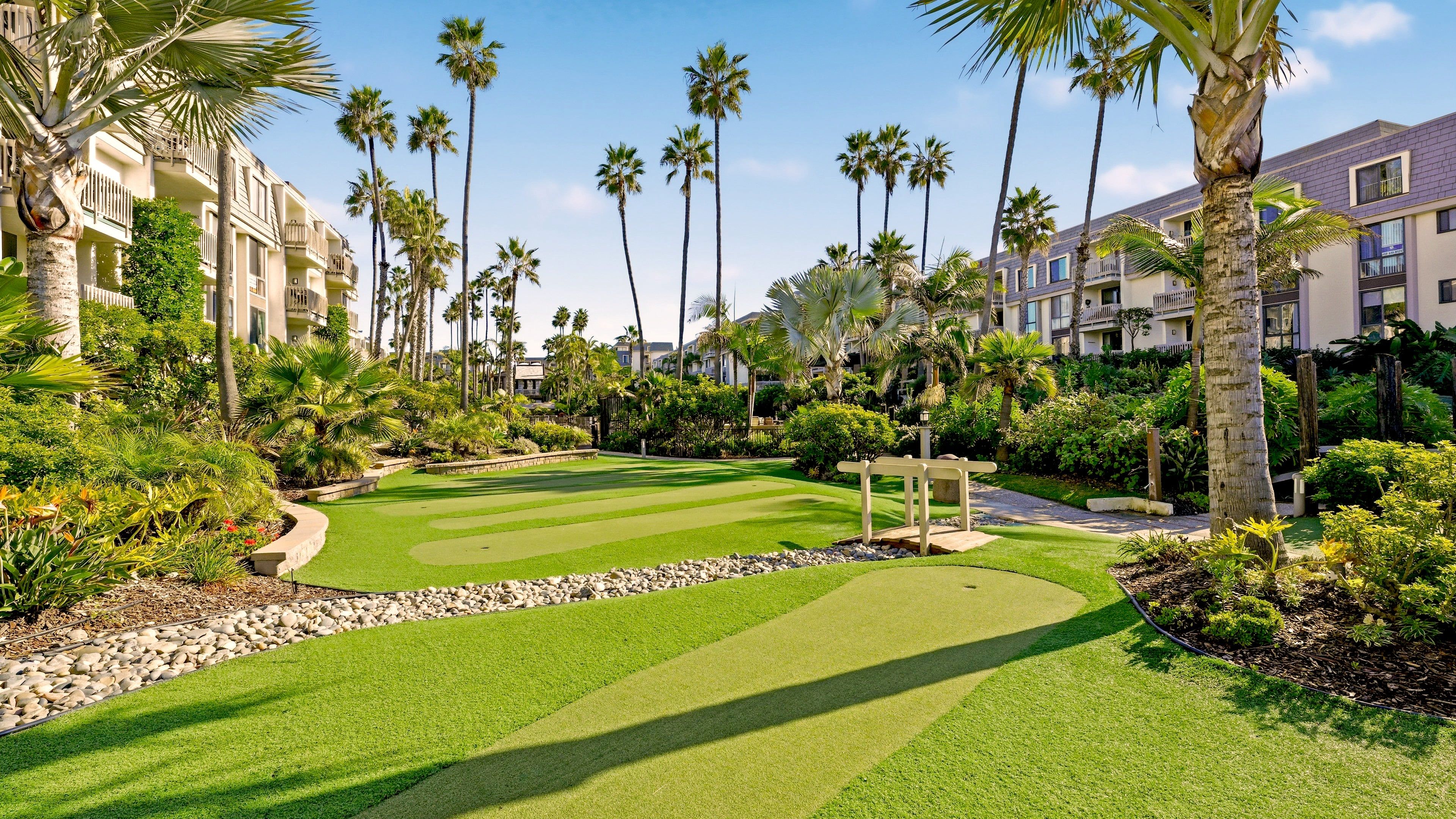 A golf course with a putting green, surrounded by palm trees and a building with balconies.