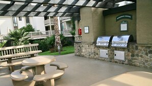 An outdoor barbecue area with stone walls, a grill, and picnic tables.
