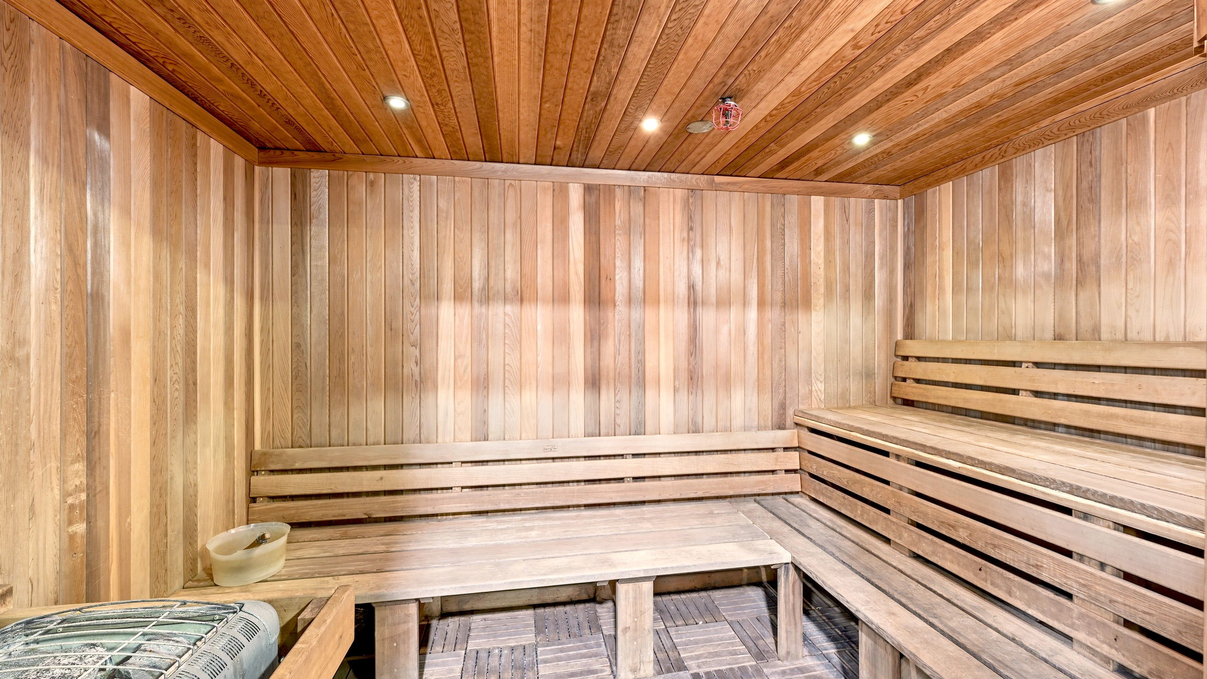 A sauna room with wooden benches and a table, wooden walls, and a sloped ceiling with recessed lighting.