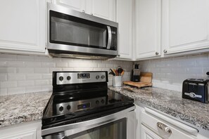A kitchen with white cabinets, a stainless steel microwave, a black stove, and a toaster.