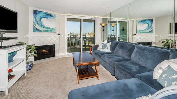 A living room with a blue sofa, a fireplace, a TV, and artwork on the walls.