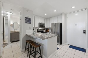A modern kitchen with white cabinets, a granite countertop, stainless steel appliances, and a bar stool.